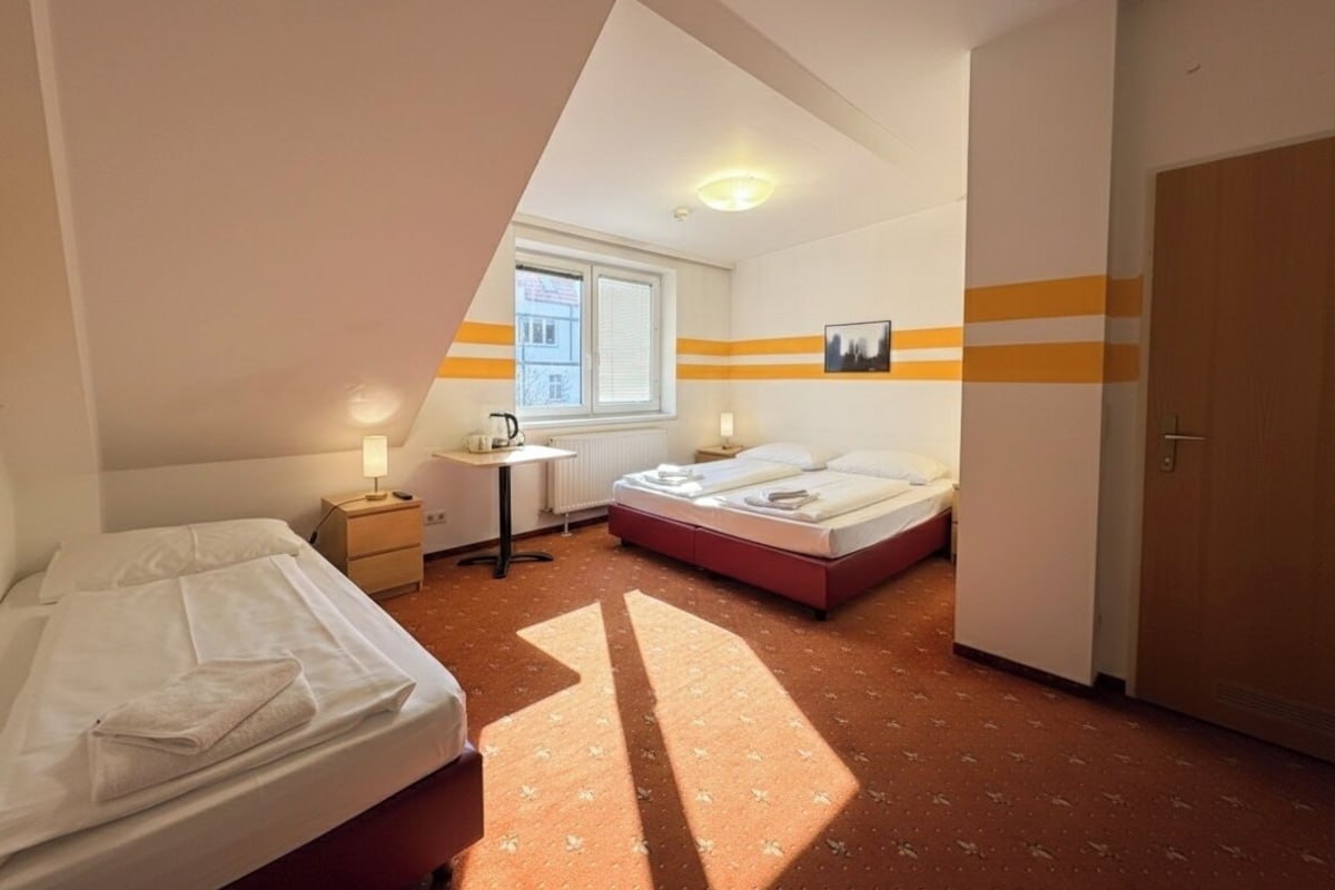 Un dormitorio con dos camas, una mesita de noche con lámpara, una ventana y una puerta.