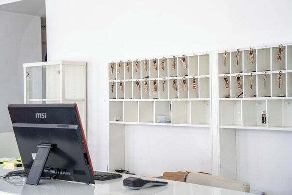 A desk with a computer, a keyboard, a mouse, and a calculator. There are shelves with keys and a white wall in the background. - Hotel Alser (Vienna)