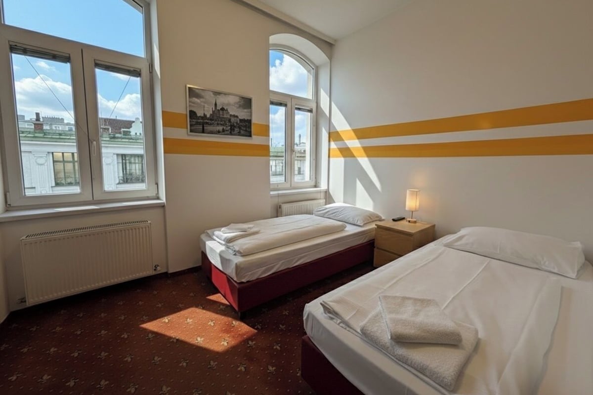 Habitación de hotel con dos camas, una ventana con vistas a la ciudad, un radiador y un cuadro en la pared.