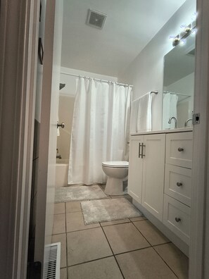 A bathroom with a toilet, a shower curtain, a sink with a mirror, and a tiled floor.