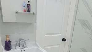 Un bagno con lavandino bianco, un water, box doccia in vetro e una porta con portascope sopra.