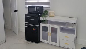 Una stanza con un armadio bianco, un frigorifero nero, un forno a microonde e una porta che dà su un'altra stanza.