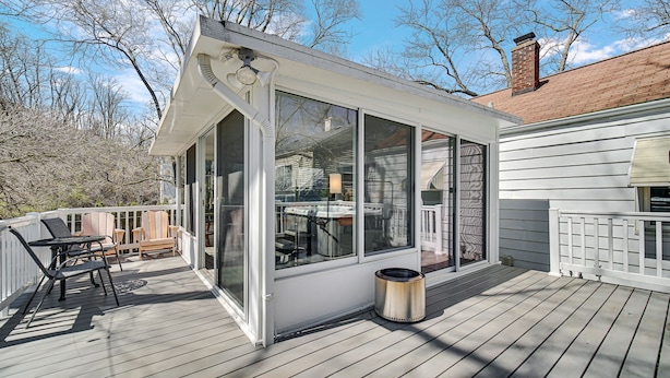 Une terrasse couverte avec une structure en verre, une poubelle en métal et du mobilier d’extérieur.