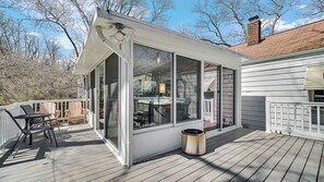 Eine überdachte Terrasse mit Glasverkleidung, einem Metallmülleimer und Gartenmöbeln.