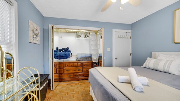 Ein Schlafzimmer mit Bett, Kommode, Kleiderschrank und einem Fenster mit Jalousien.