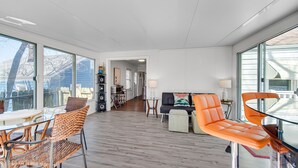 Un vaste espace de vie doté d’une grande fenêtre, d’une table à manger, de chaises en osier, d’un canapé et d’un fauteuil orange vif.