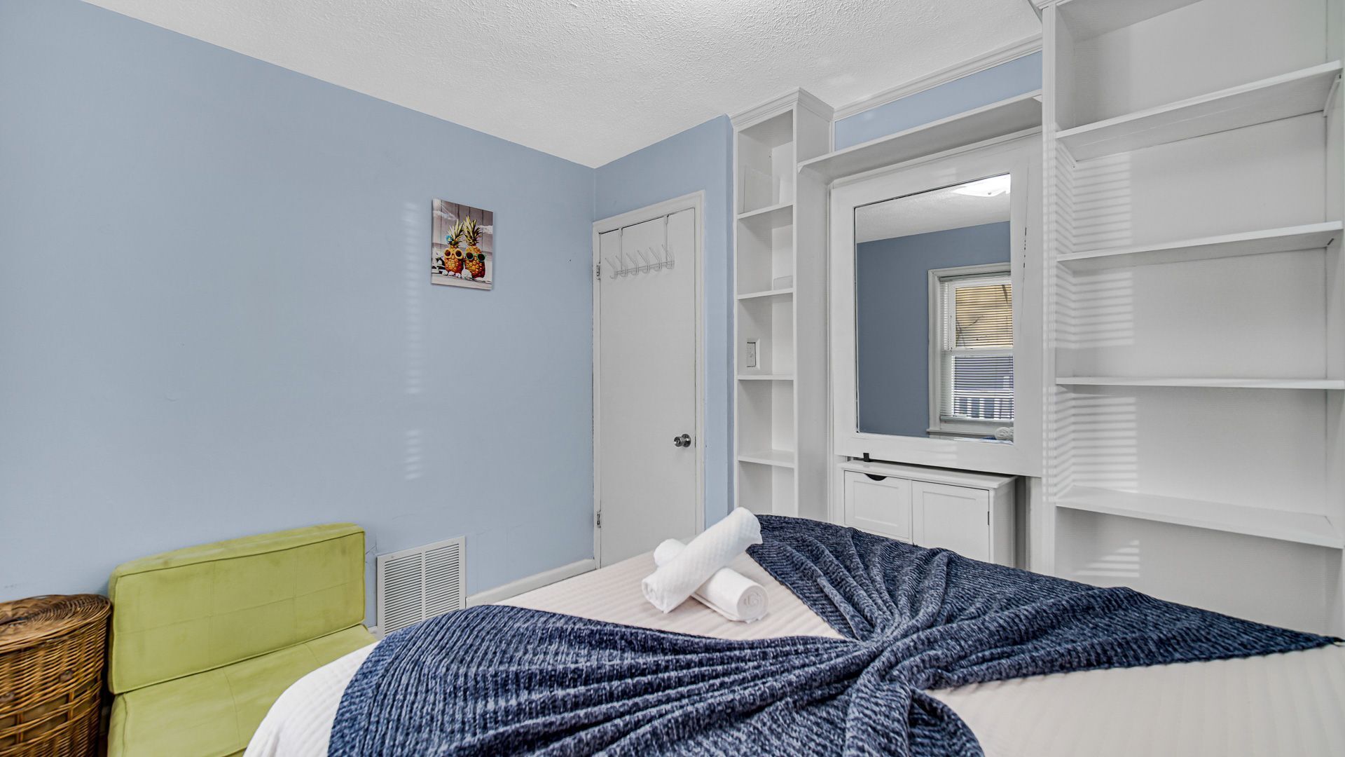 A bedroom with a bed, a green chair, a white wardrobe, and a mirror.