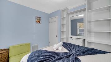 A bedroom with a bed, a green chair, a white wardrobe, and a mirror.