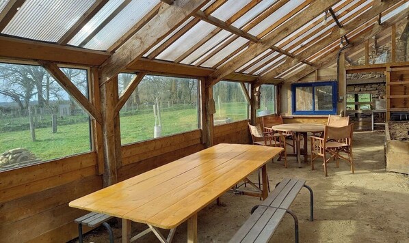Un coin repas rustique en bois, avec une longue table et des bancs, de grandes fenêtres et une cheminée en pierre.