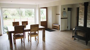 Ein geräumiges Wohnzimmer mit Esstisch und Stühlen aus Holz, einem Kamin und großen Fenstern mit Blick ins Freie.