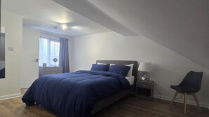 Ein Schlafzimmer mit Bett, Nachttisch, Lampe, Stuhl und Blick ins Freie durch ein Fenster.