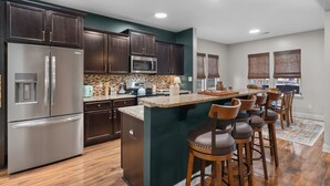 A modern kitchen with dark wood cabinets, stainless steel appliances, and a central island with bar stools. - Privacy in the Pines + Hot Tub +Custom Fire Pit (Aberdeen)