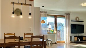 Amplia sala de estar con una mesa de comedor de madera, sillas, televisor y un ventanal con cortinas.