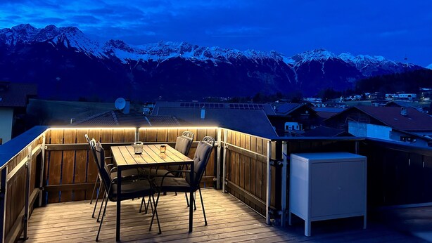 Una terraza de madera con una mesa y sillas, con vista a una cadena montañosa nevada.