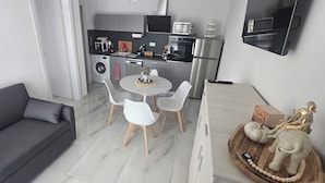 A compact living space with a grey sofa, a round dining table with white chairs, a kitchen area with modern appliances, and a decorative elephant figurine. - DaRo- Appartments - APP FYNN (250m to the beach) (Serraiki Akti)