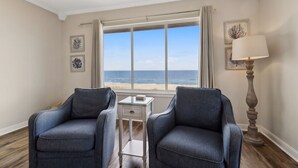 Ett rum med två fåtöljer, ett litet bord, en lampa och utsikt över havet.