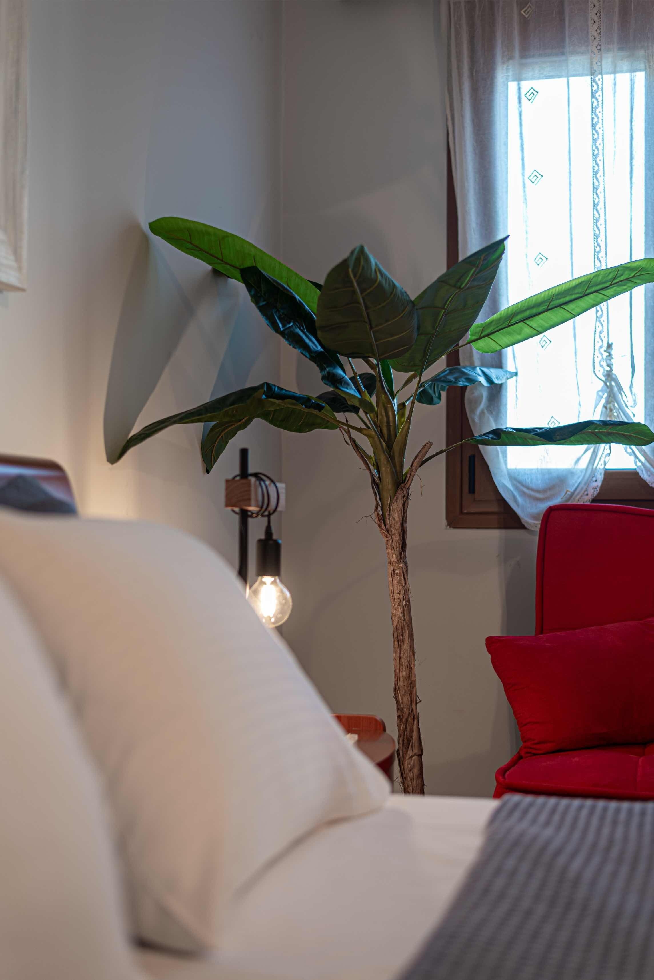 A room with a bed, a red chair, a potted plant, and a wall-mounted light fixture.