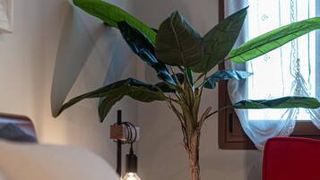 A room with a bed, a red chair, a potted plant, and a wall-mounted light fixture.
