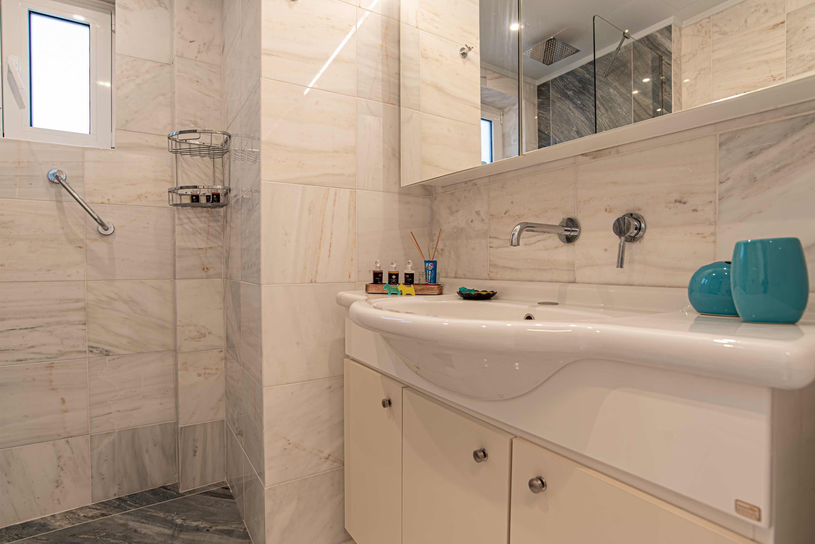 Une salle de bain moderne avec une douche dont le sol et les murs sont recouverts de carreaux de marbre, un lavabo blanc avec un miroir au-dessus, et un porte-savon contenant des articles de toilette.