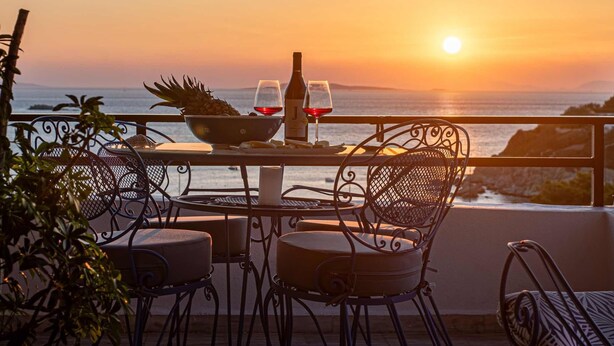 A terrace with a table set for two, overlooking a sunset over the sea. - Feliz Apt- Breathtaking Seaview and Sunset by ΜΡS (Anavissos)