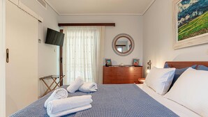 A neatly made bed with blue bedding, a wooden dresser, a round mirror, and a painting on the wall. - Feliz Apt- Breathtaking Seaview and Sunset by ΜΡS (Anavissos)