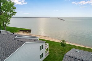 A residential area with a view of a calm body of water, a sandy beach, and a wooden pier.