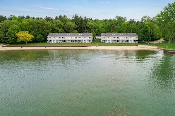 A waterfront property with two multi-story buildings, a sandy beach, and a forested area in the background.