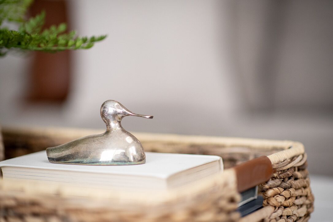 A silver duck-shaped object on a stack of books, placed on a woven basket.