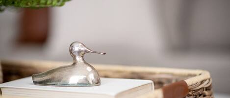 A silver duck-shaped object on a stack of books, placed on a woven basket.