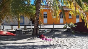 En sandstrand med ett palmträd och en byggnad med orangefärgade väggar.