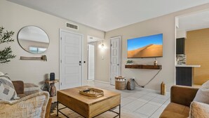 A living room with a wooden coffee table, brown sofas, a round mirror, and a television displaying a desert landscape.