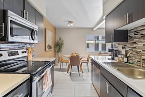 A modern kitchen with a built-in microwave, stove, and oven. There is a dining table with chairs and a potted plant.