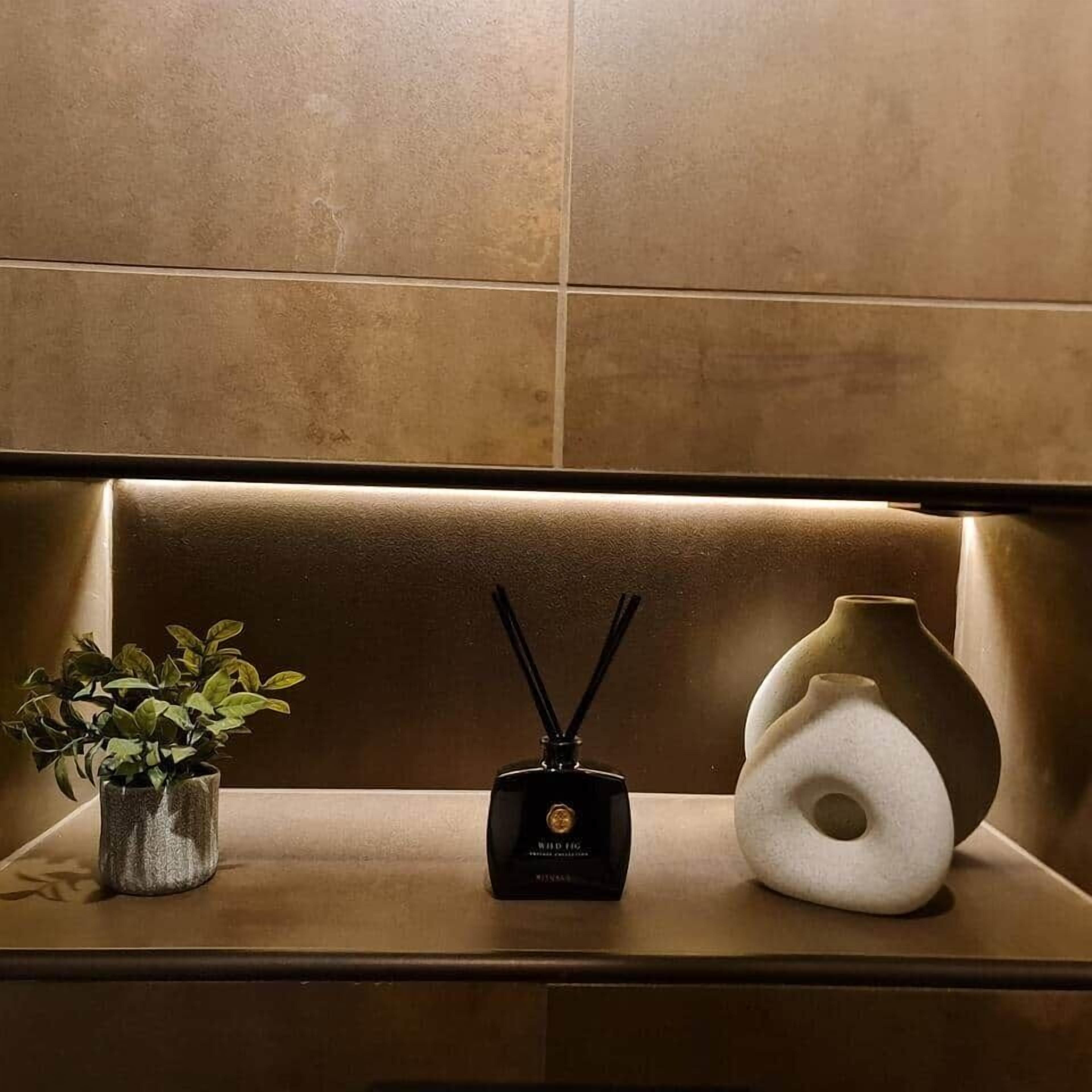 A shelf with a potted plant, a black diffuser, and a white vase.
