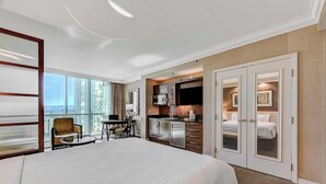 A hotel room with a large bed, a dining table, a kitchen area, and a view of the city. - Luxurious Tower 3 Studio | Pool + Strip View (Las Vegas)