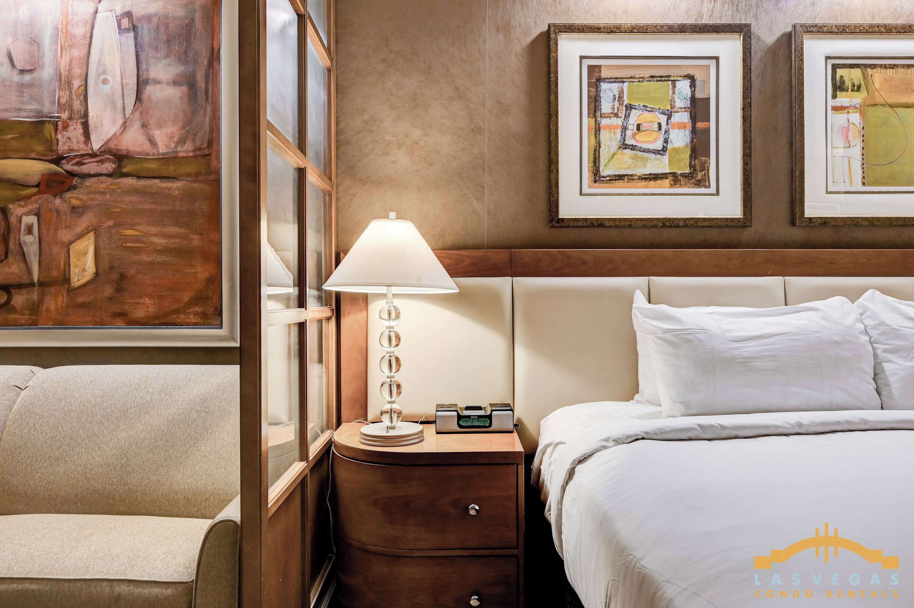 Une chambre d’hôtel avec un lit, une table de chevet avec une lampe, une chaise et des œuvres d’art accrochées aux murs.