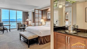 Une chambre d’hôtel avec un grand lit, deux fauteuils, une petite table et une vue sur le paysage urbain.
