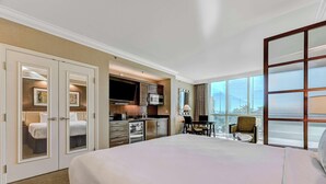 Habitación de hotel con cama, kitchenette, zona de comedor y un amplio ventanal con vistas.