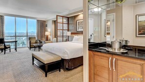 Ein Hotelzimmer mit einem großen Bett, einer Sitzecke mit Tisch, einer Küchenzeile und Blick auf die Stadt.