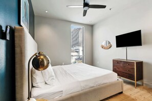 Ein modernes Schlafzimmer mit Bett, Kommode, Fernseher und Deckenventilator.