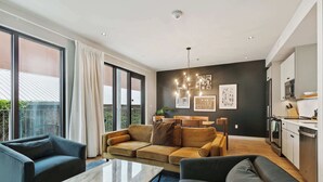 A modern living room with a sofa, armchairs, and a coffee table. There is a kitchen area with appliances and a dining table. Large windows provide natural light and a view of the outside. - Walkable 3BR Apartment w/ Balcony | Near Bourbon St + Superdome (New Orleans)