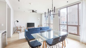 A modern living room with a glass dining table, blue sofa, and a TV. - Sleek 2 BR Apartment | Near Bourbon St. + Superdome (New Orleans)