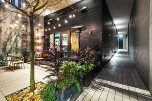 Un patio interior con zona de comedor, plantas en macetas y luces colgantes.