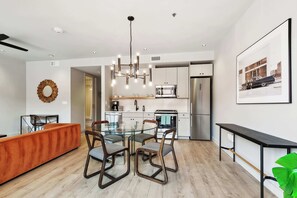 A modern kitchen with a central island, stainless steel appliances, and a dining area with a glass table and chairs. - Central 1BR Apartment in CBD w/ Balcony (New Orleans)