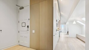 A modern interior with a wooden door, a white wall, and a hallway leading to a dining area. - Modern 2BR in Historic Schoolhouse | Gated Parking | Near Superdome (New Orleans)