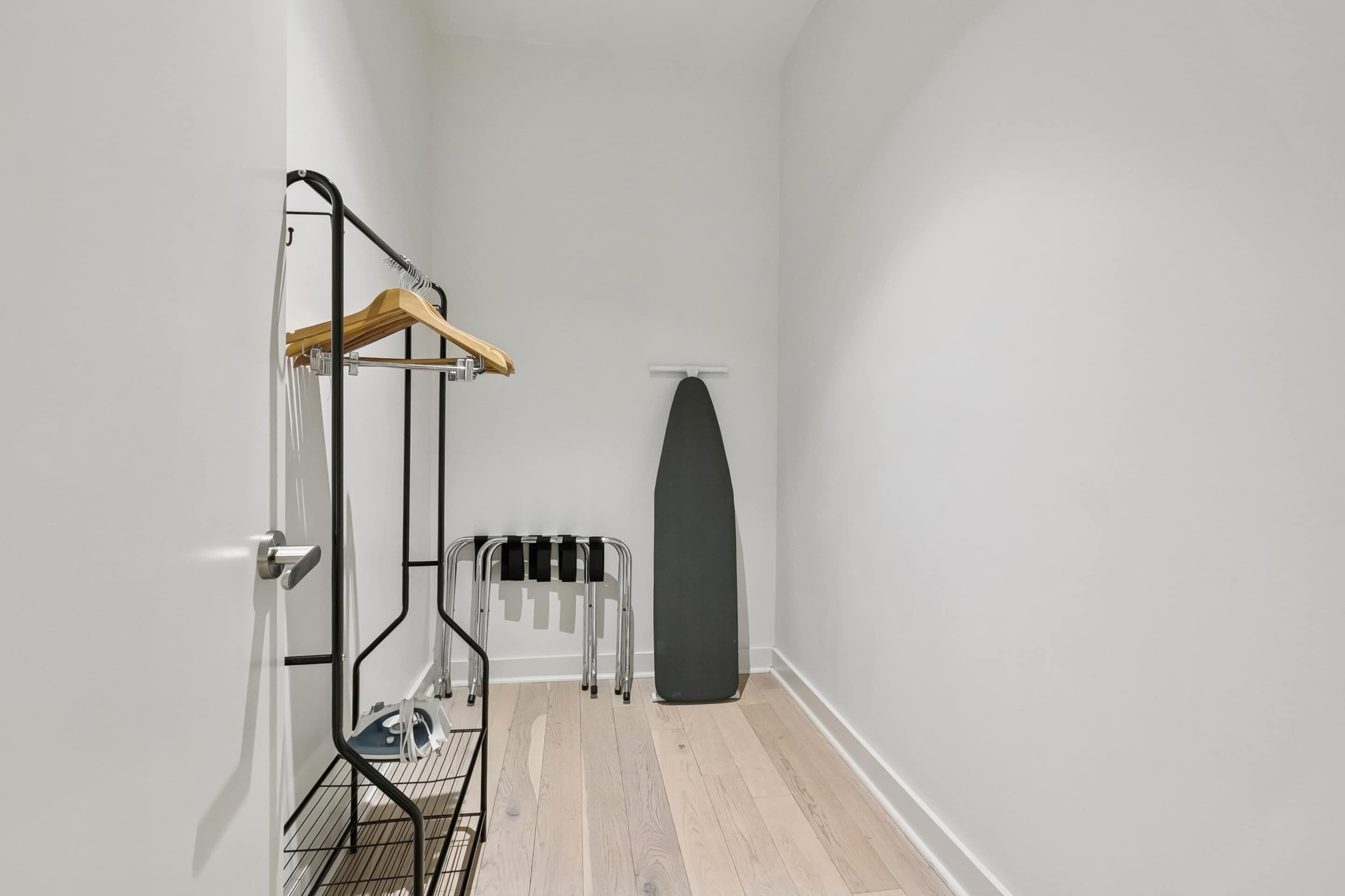 A narrow hallway with a wooden hanger, a black ironing board, and a metal rack.