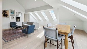 A spacious loft with a high ceiling, skylights, a dining area with a wooden table and chairs, a sofa, and a coffee table. - Modern 2BR in Historic Schoolhouse | Gated Parking | Near Superdome (New Orleans)