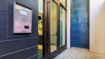 A modern elevator with a control panel, glass doors, and a tiled floor.