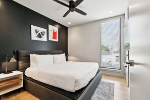 Ein modernes Schlafzimmer mit einem großen Bett, einem Deckenventilator und einem Fenster mit Jalousien.