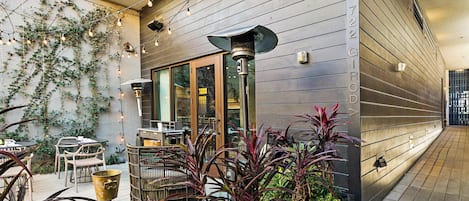 An outdoor patio with tables and chairs, a metal trash bin, and a planter with various plants.
