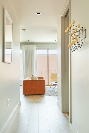 Ein Flur mit einem modernen orangefarbenen Sofa, einer geometrischen Wanddekoration und Blick auf einen Balkon mit einem Stuhl.